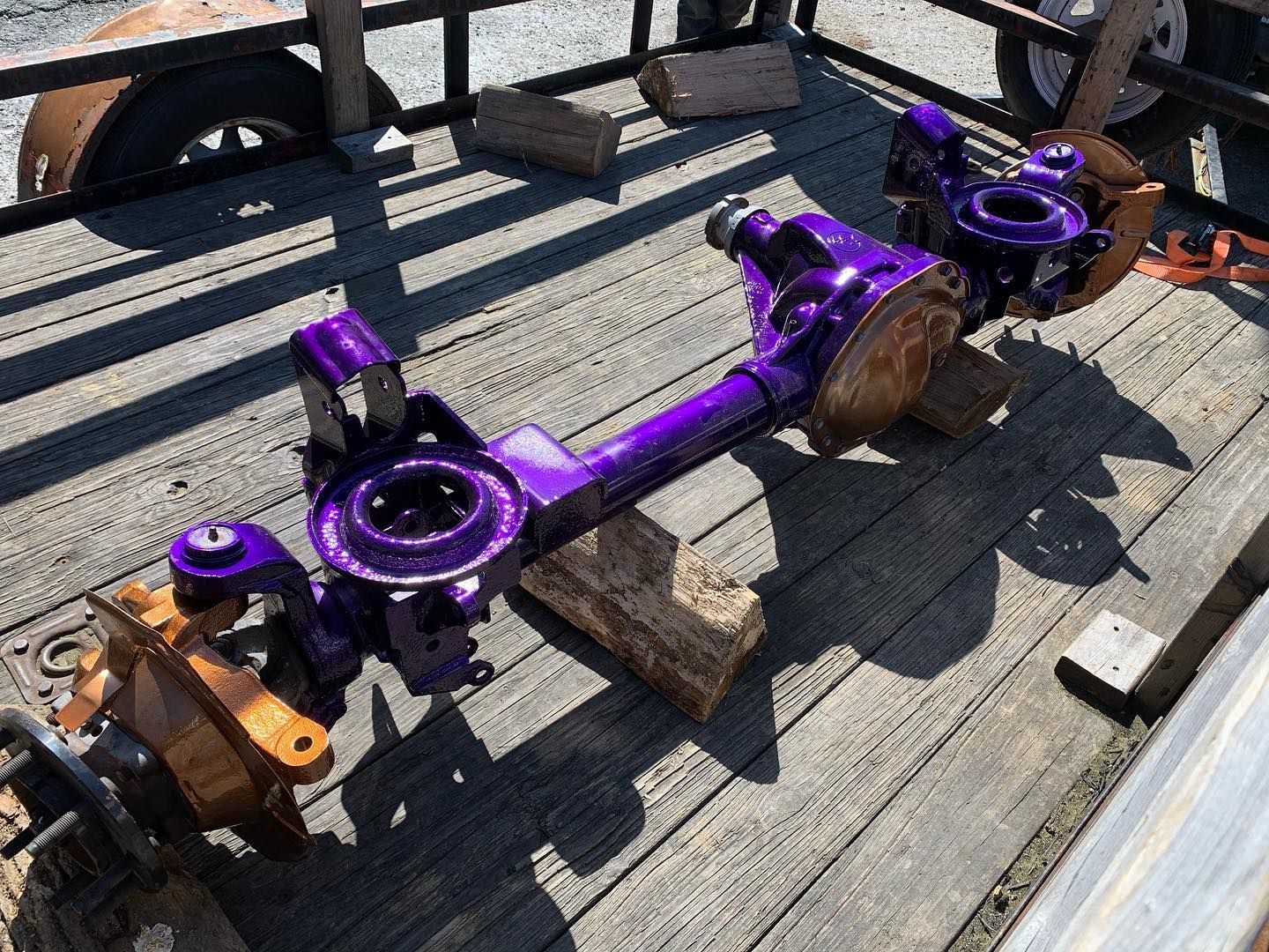 A bright purple car axle sits on wooden blocks on a trailer bed. A bright purple car axle sits on wooden blocks on a trailer bed.