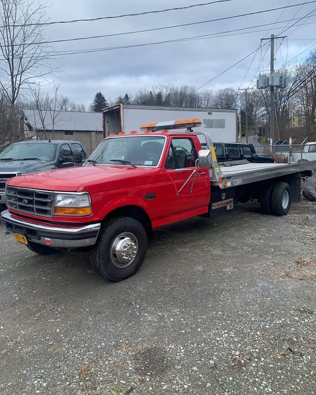 Red tow truck parked on gravel, with a flatbed and an orange light bar.