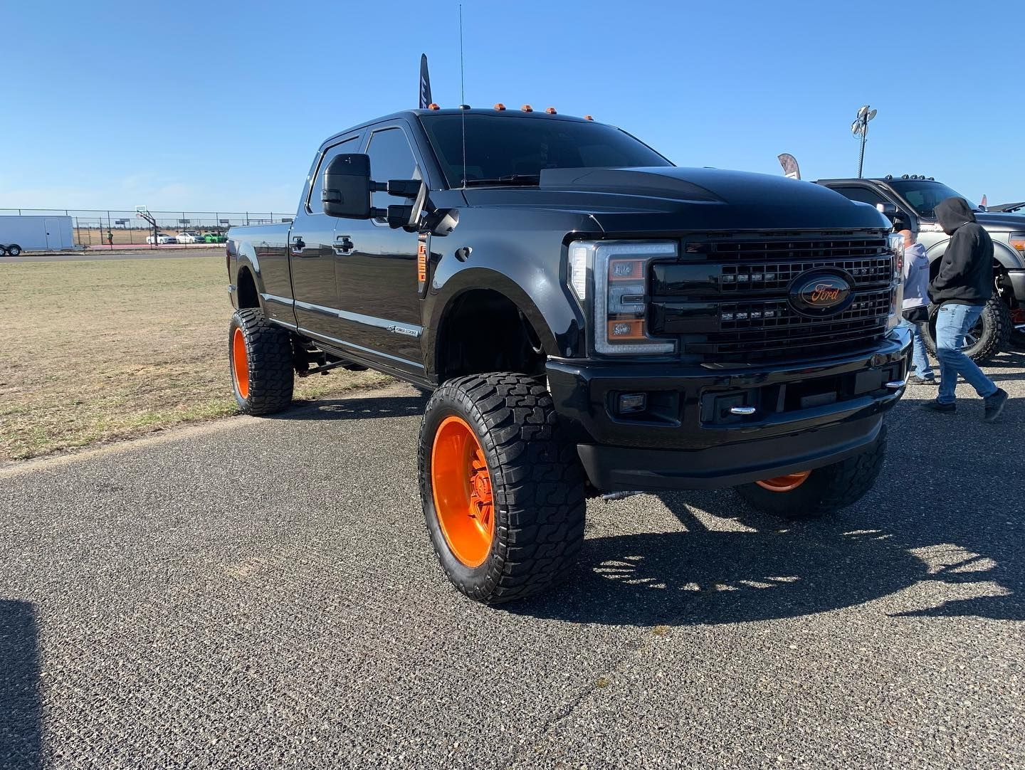 Black lifted truck with orange wheels, parked on asphalt on a sunny day. Black lifted truck with orange wheels, parked on asphalt on a sunny day.