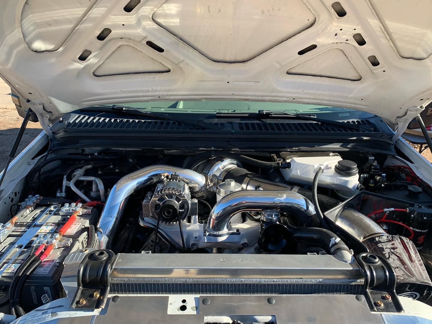 Open hood of a white truck, revealing a customized engine with chrome components. Open hood of a white truck, revealing a customized engine with chrome components.