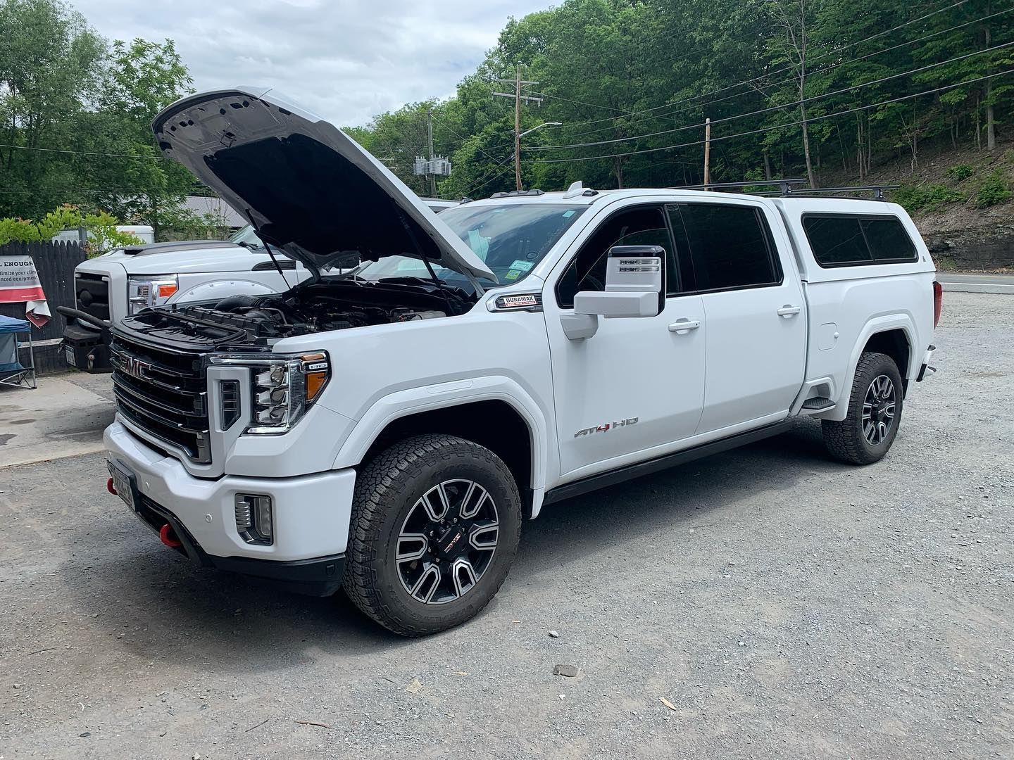 White GMC truck with hood open, parked outdoors on gravel.