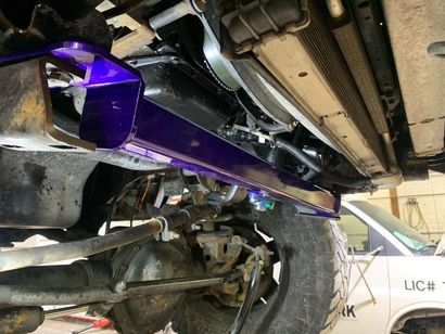Underside of a vehicle, showing a purple-painted metal part, suspension components, tire, and radiator.