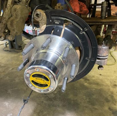 A shiny metal wheel hub with a yellow WARN emblem attached to a vehicle's front suspension.