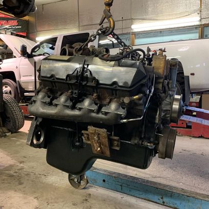 Engine suspended from a hoist in a garage, near a white truck.