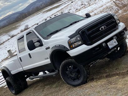 White lifted pickup truck with black trim, wheels, and tinted windows, parked on brown grass with a snowy mountain background.