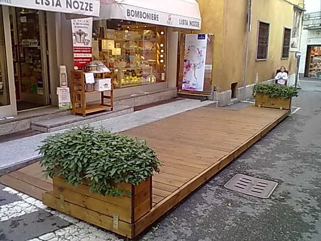 Piattaforma pedonale in legno con piante in vaso davanti ai negozi in una via stretta
