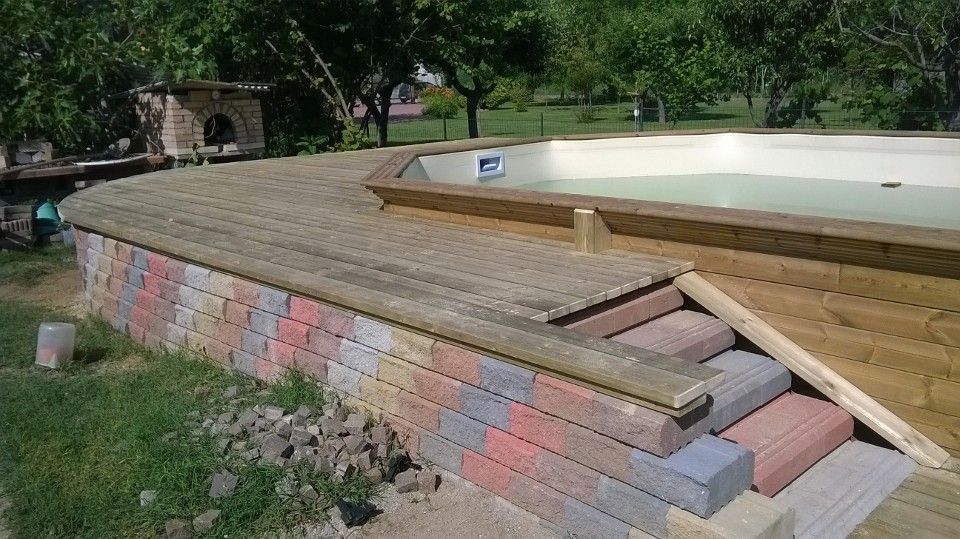 Terrazza della piscina parzialmente costruita con assi di legno e tavole sovrapposte accanto a un muro di contenimento in mattoni.