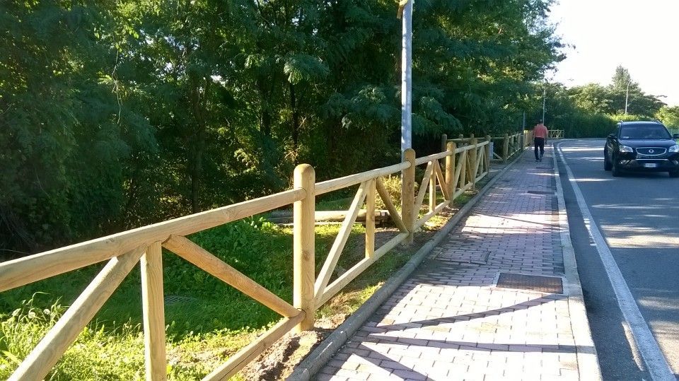 Marciapiede con ringhiera in legno a lato di una strada, con alberi e un'auto sullo sfondo.