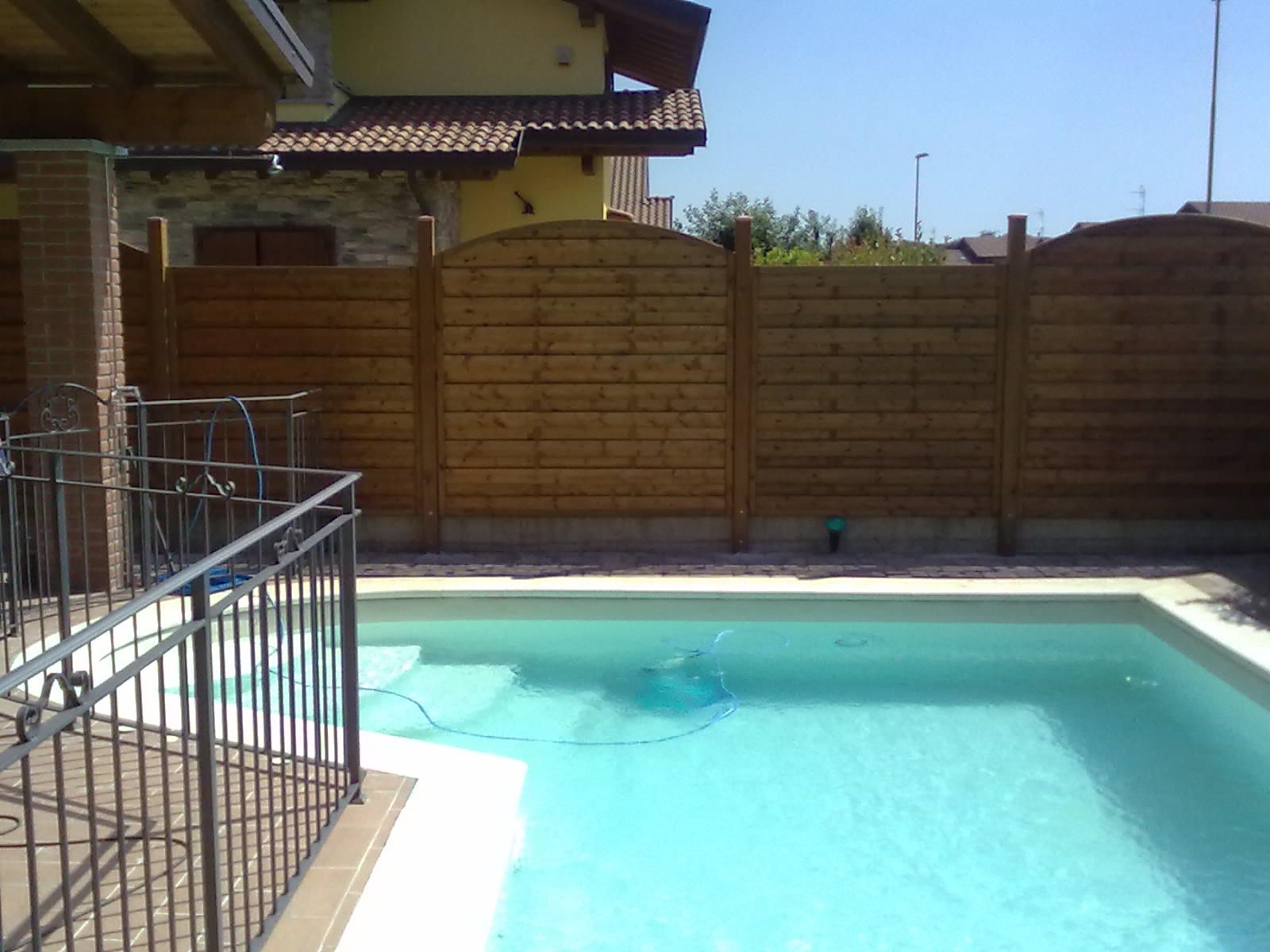 Piscina in giardino con acqua turchese, recinzione in legno e ringhiera del patio sotto un cielo limpido