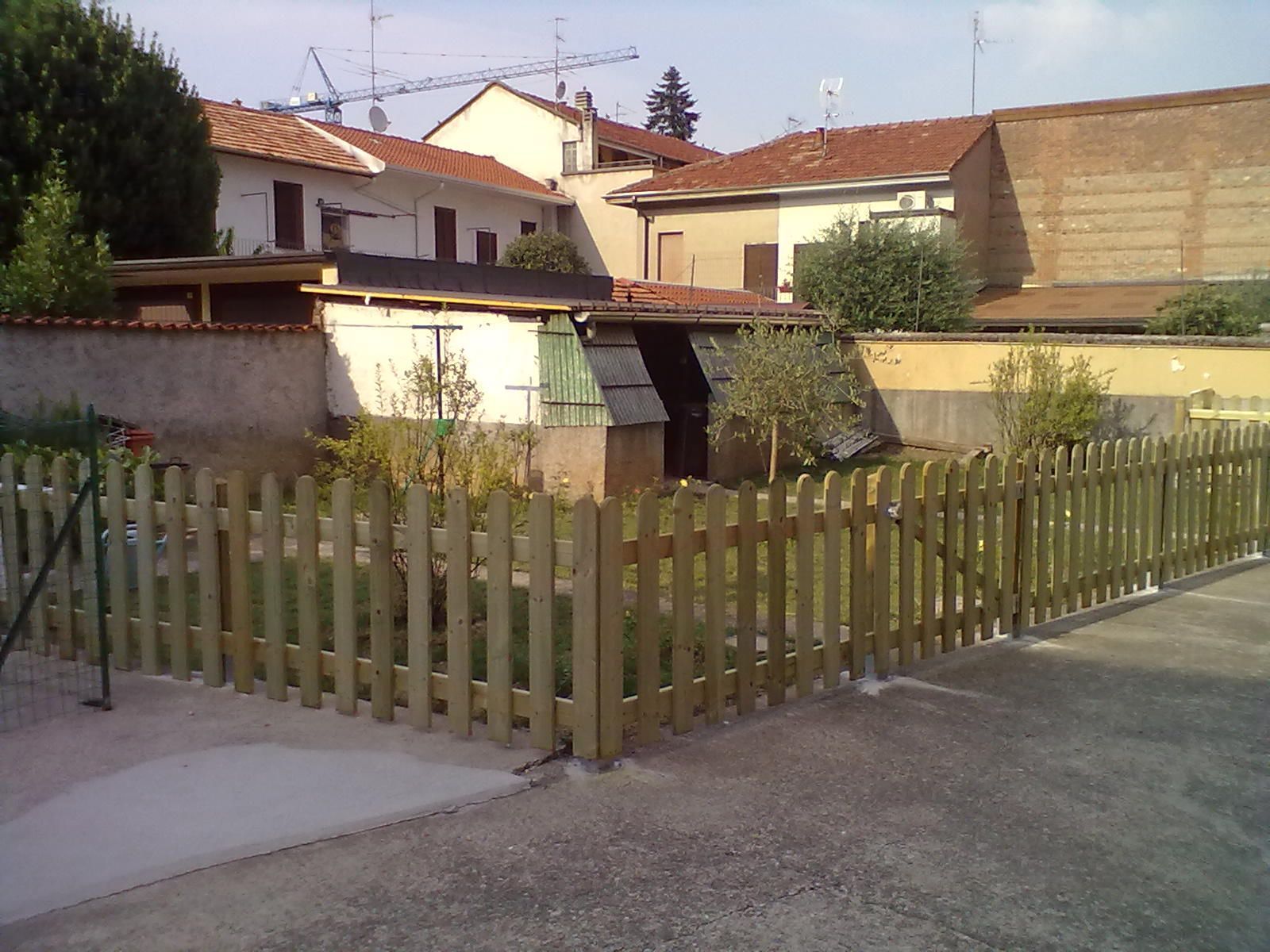 Casa di periferia dietro una recinzione di legno con un piccolo giardino e un vialetto d'accesso sotto un cielo limpido