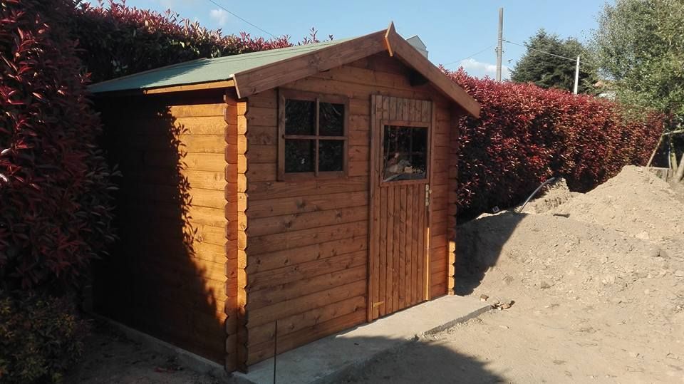 Una piccola casetta di legno con due finestre, situata accanto a un cumulo di terra e ad alte siepi rosse.