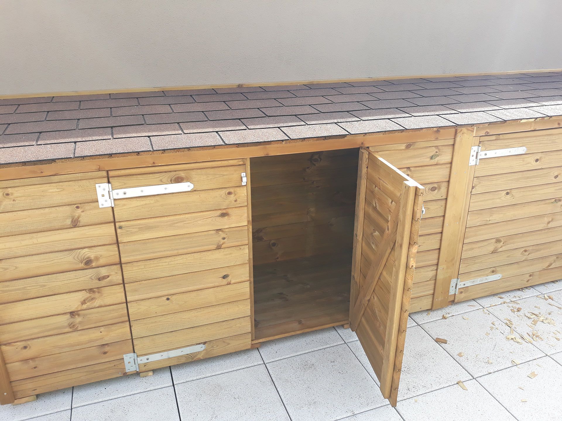 Armadio in legno per esterni con un'anta aperta, che lascia intravedere l'interno vuoto.