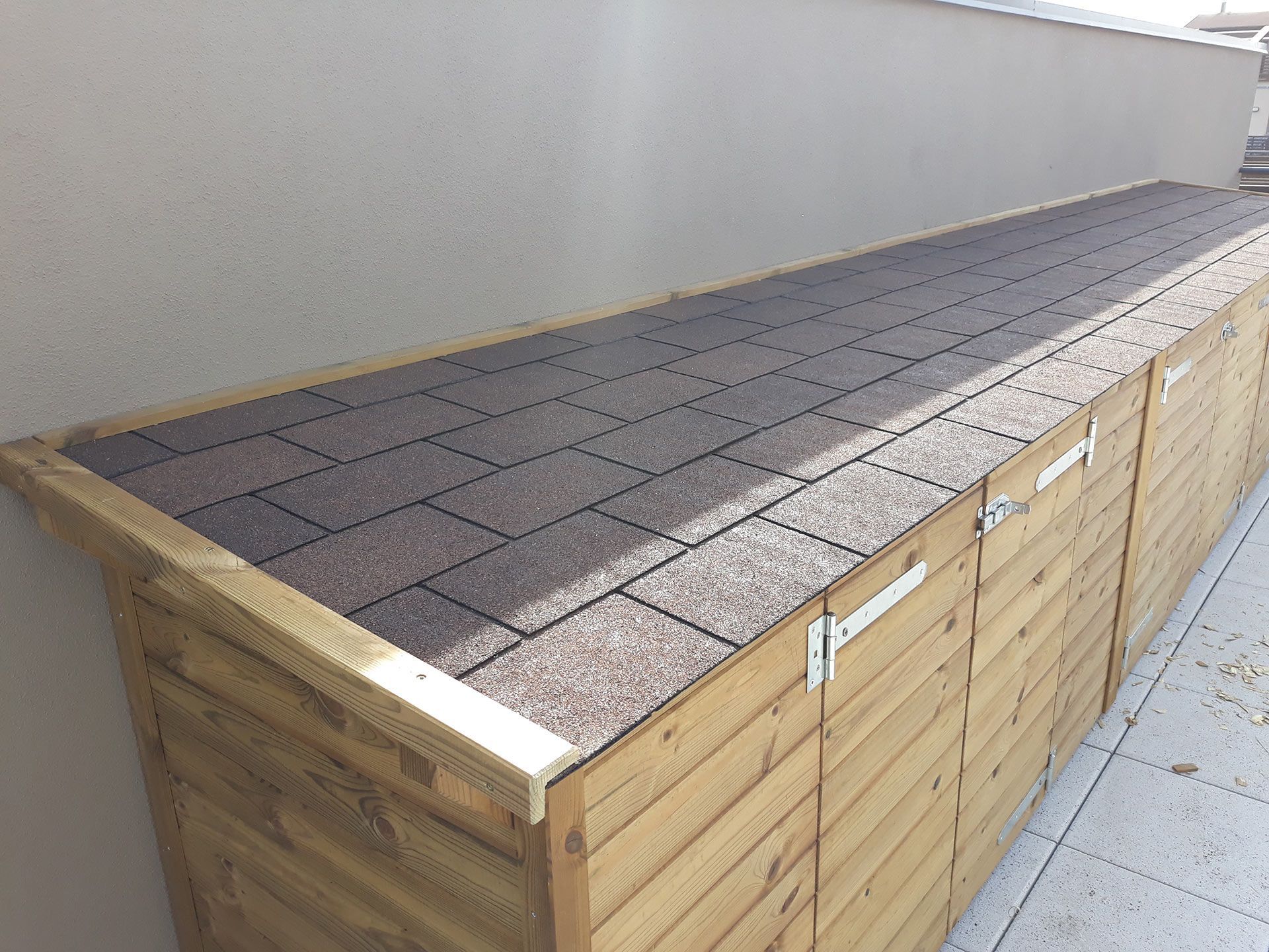 Panca contenitore in legno con coperchio a tegole accanto a un muro esterno
