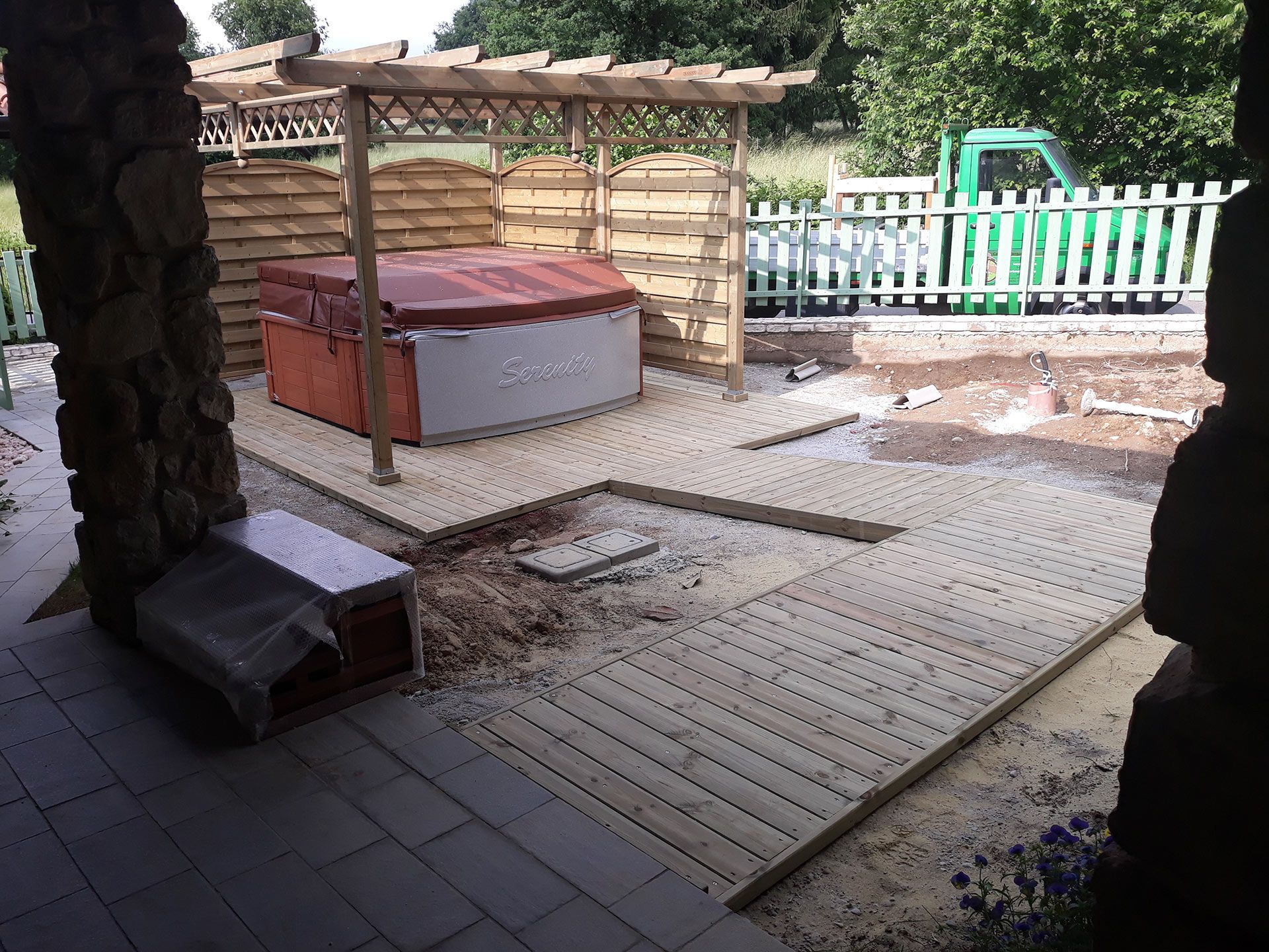 Patio sul retro con terrazza in legno, vasca idromassaggio coperta, panchina e giardino recintato.