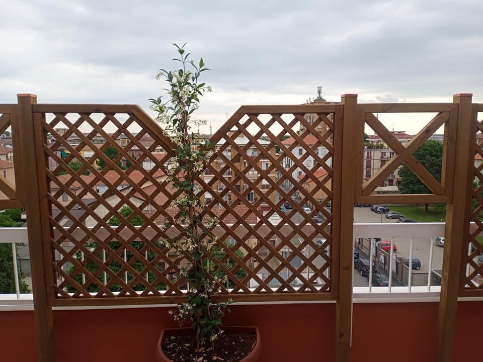 Ringhiera in legno a traliccio per balcone con piante in vaso e case visibili oltre
