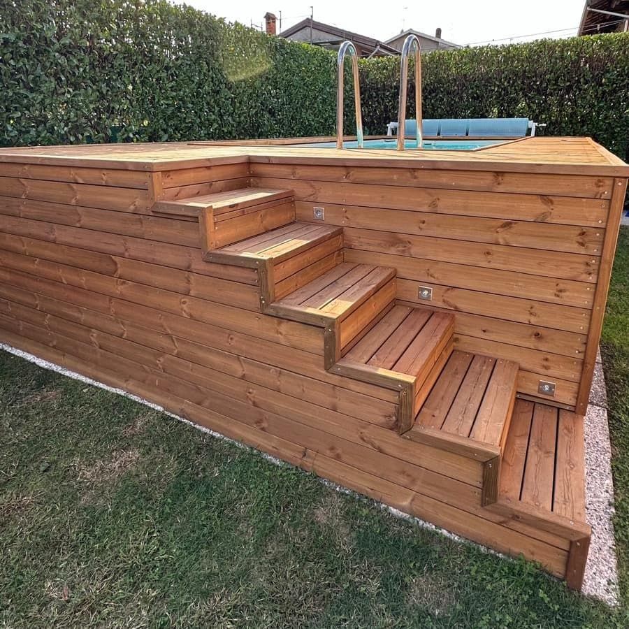 Terrazza in legno per la piscina nel cortile sul retro, con scalini integrati e recinzione delimitata da siepi.