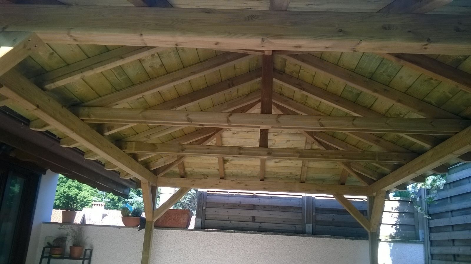 Gazebo in legno con tetto a vista e parte inferiore tinta di verde, situato in un patio esterno.
