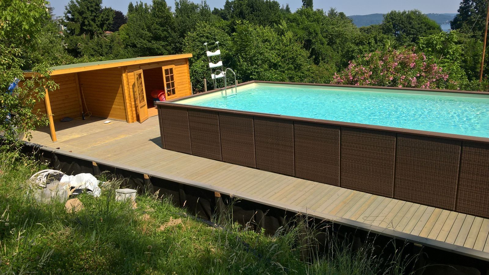 Piscina fuori terra nel cortile con terrazza in legno e casetta gialla, circondata dal verde.