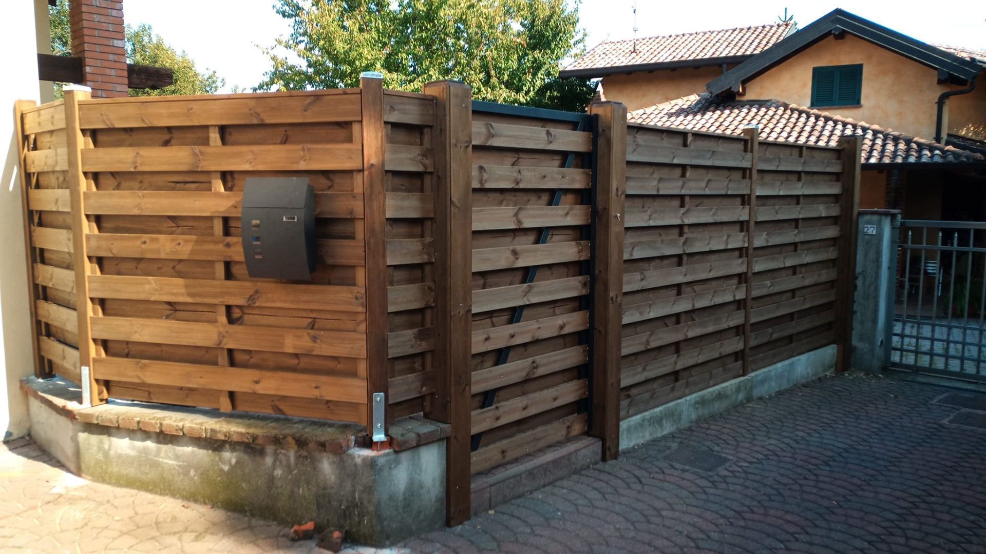 Recinzione e cancello in legno che delimitano un cortile d'angolo accanto a una casa in mattoni in una giornata di sole
