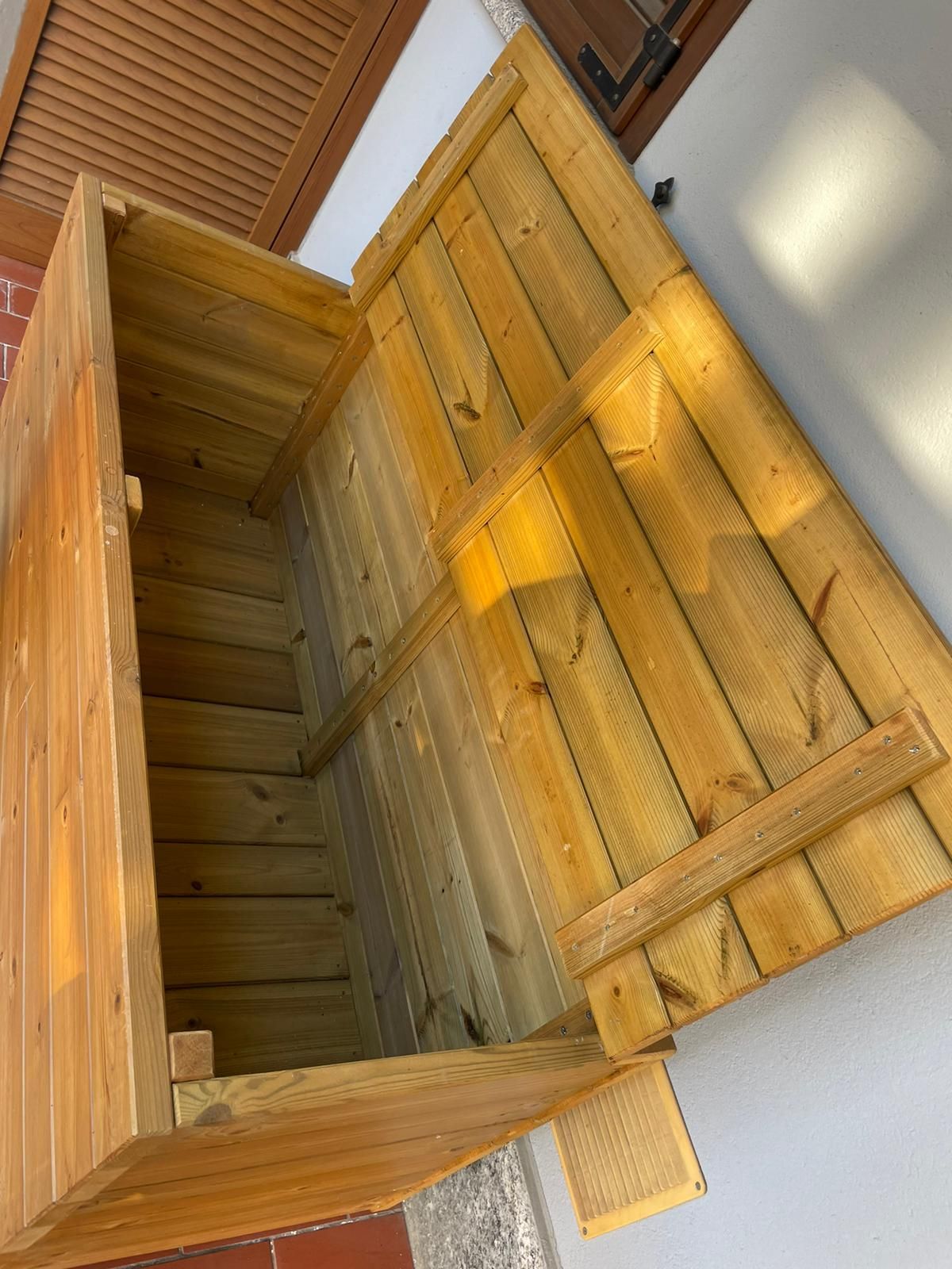 Cassapanca di legno aperta con coperchio incernierato su un pavimento piastrellato vicino a una parete