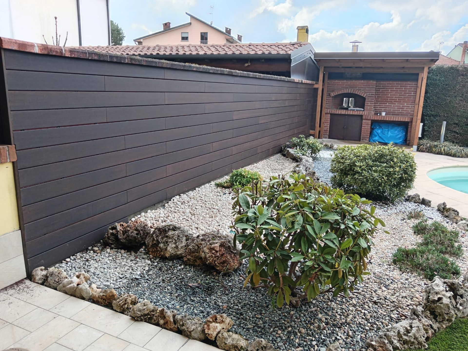 Giardino moderno con cortile interno, aiuole di ghiaia, arbusti e una recinzione in legno scuro che garantisce la privacy, adiacente a una casa.