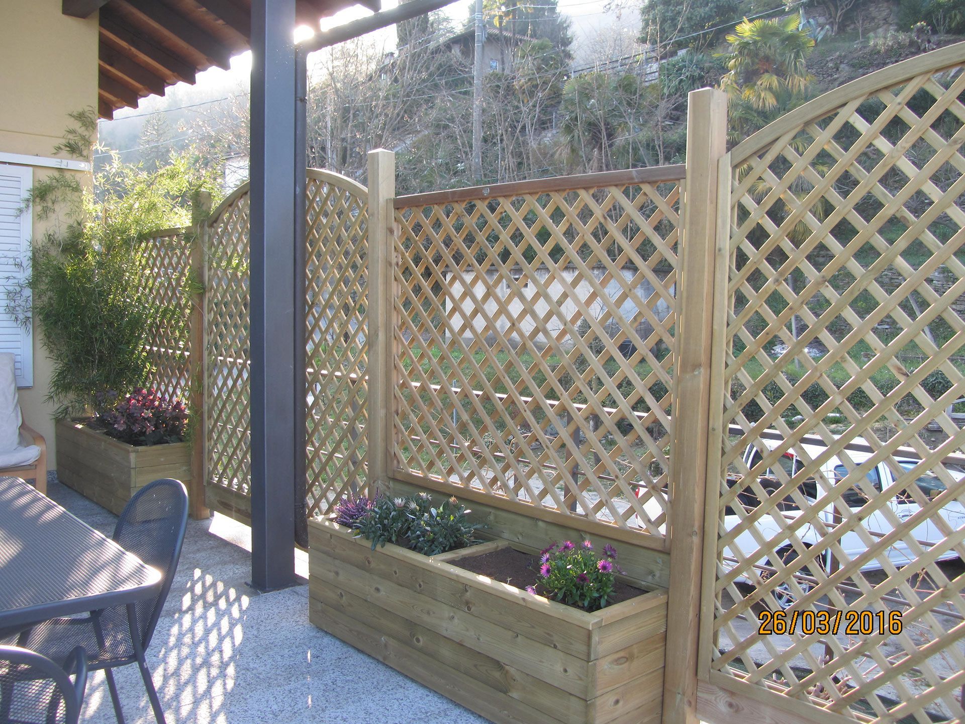 Patio con recinzione in legno a traliccio, fioriera rialzata e sedie in pieno sole