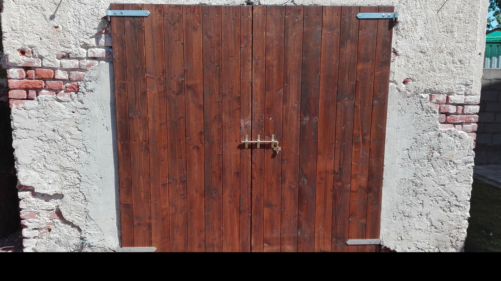 Doppia porta rustica in legno incastonata in un muro di pietra bianca grezza con bordi in mattoni e cerniere in metallo.