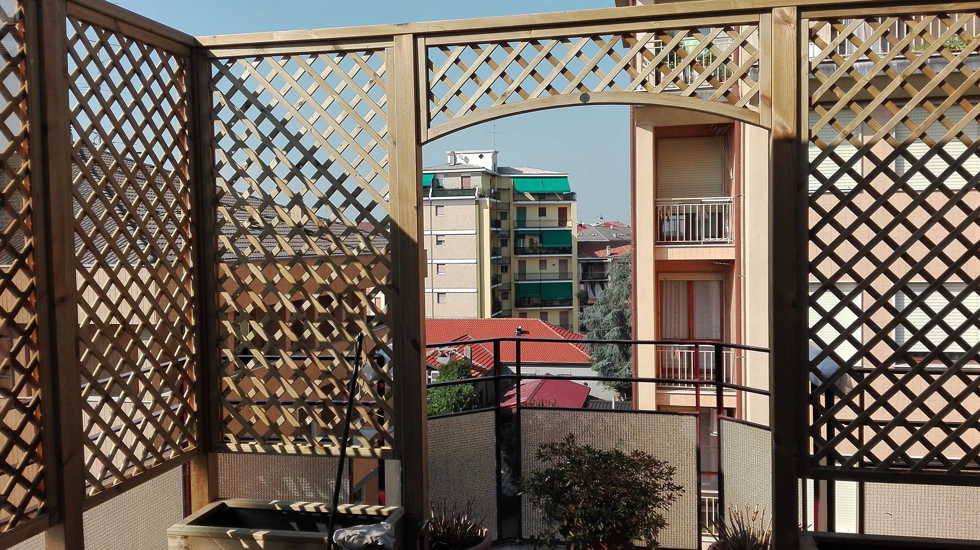 Vista attraverso un balcone con grata in legno di palazzi residenziali e una tenda da sole rossa in pieno giorno
