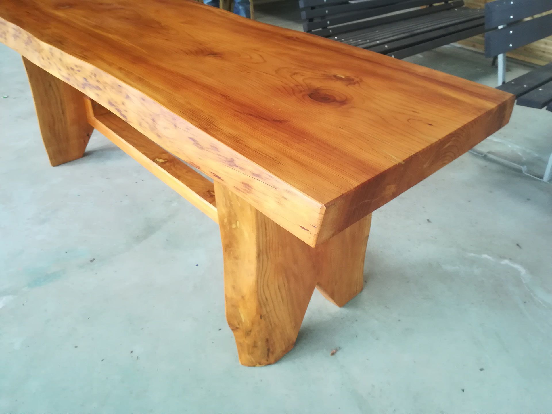 Panchina in legno con piano spesso e lucido e gambe robuste su un pavimento in cemento.