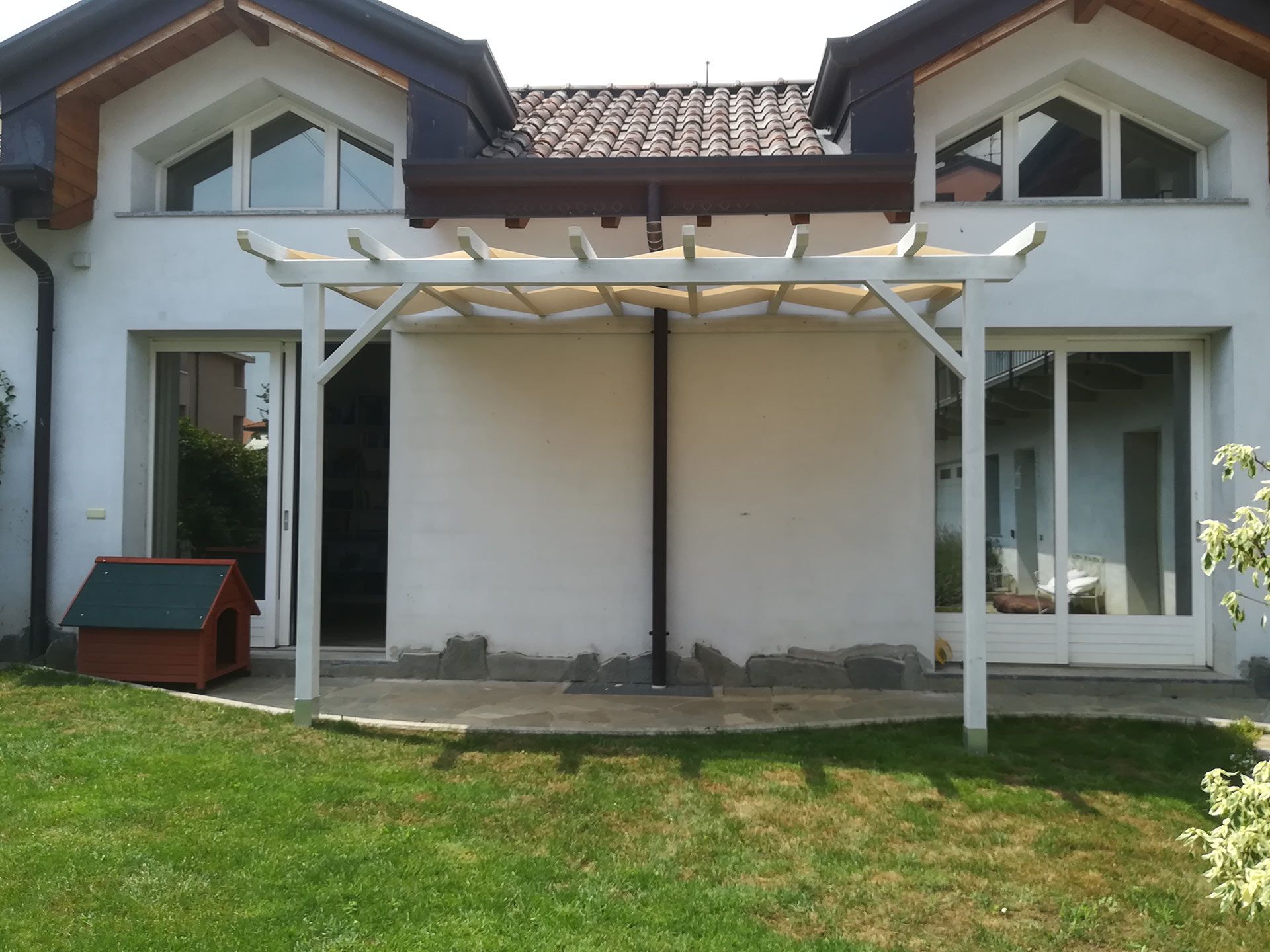 Patio della casa bianca con pergola, porte a vetri e un piccolo prato verde.