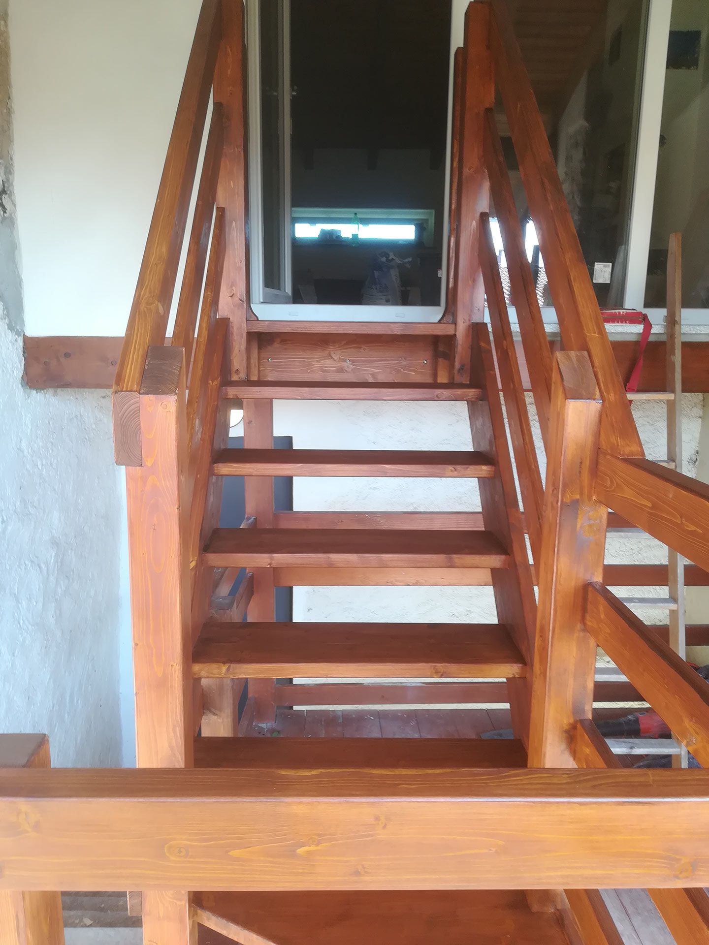 Scala in legno che conduce a una porta scura, con ringhiere lucide e pavimento piastrellato.