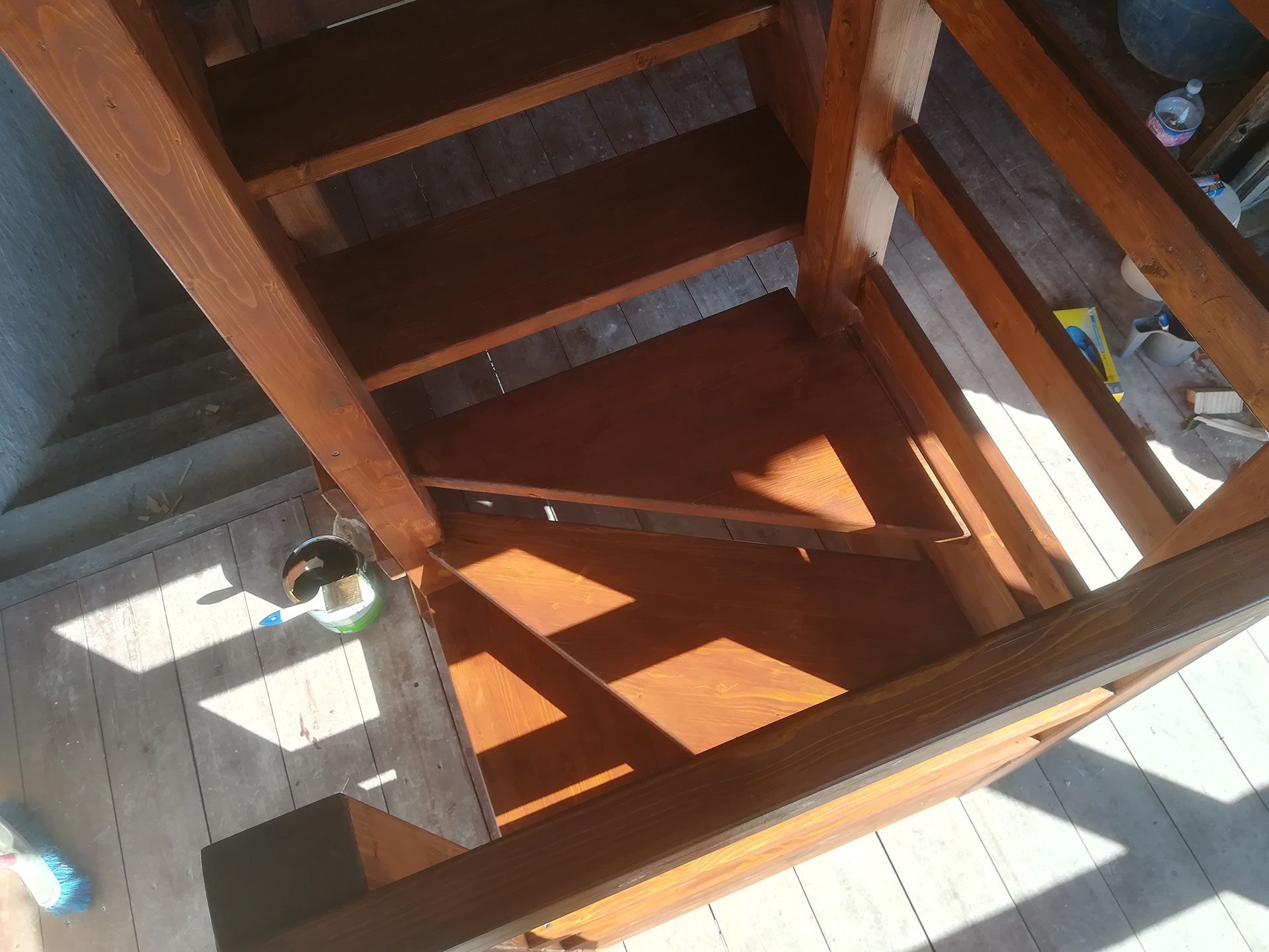 Pianerottolo di una scala in legno con giochi di luce e ombre, che mostra ringhiere e gradini dall'alto.