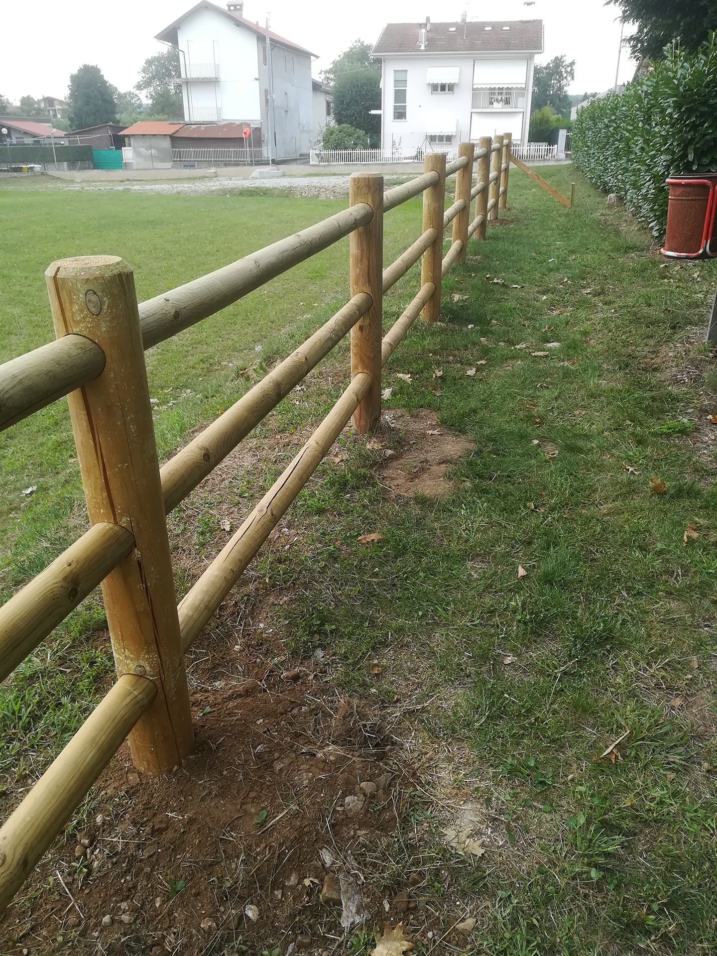 Una recinzione di legno lungo un sentiero erboso accanto alle case in una giornata nuvolosa.