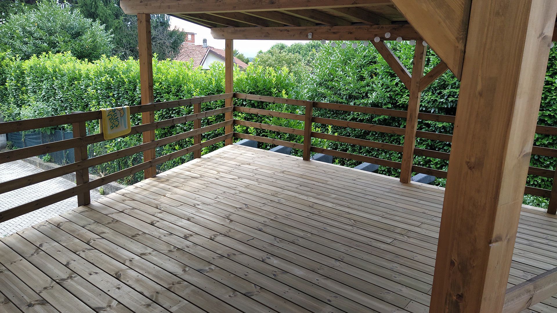 Terrazza in legno coperta con ringhiere affacciata su un giardino verde.