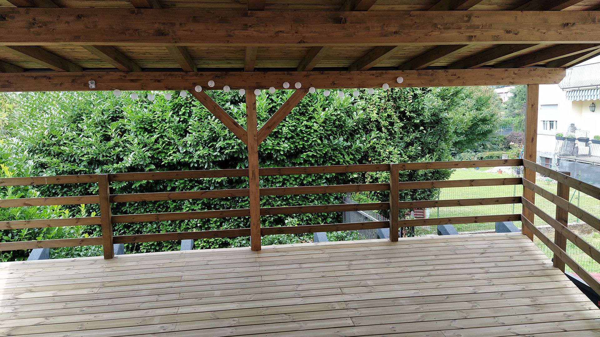 Veranda coperta in legno con vista su alberi verdi e su una collina in lontananza.