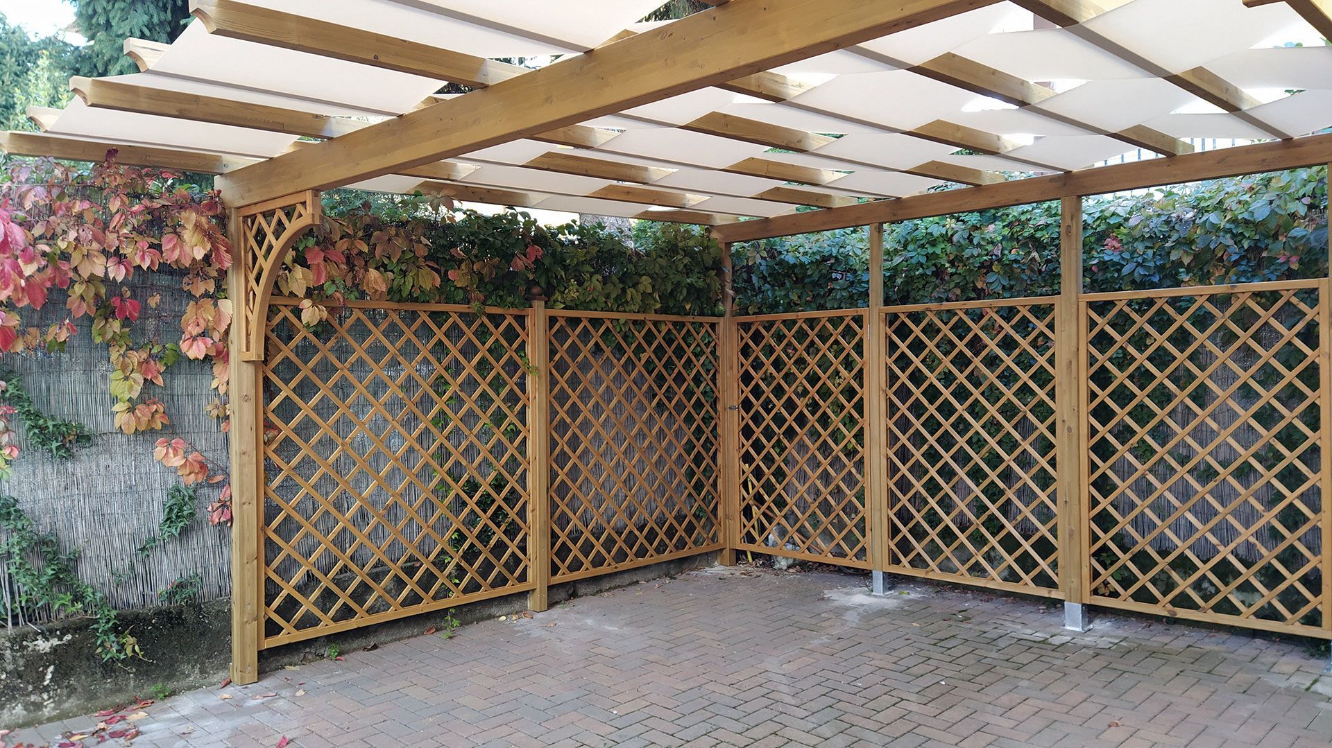 Patio coperto con pareti a traliccio in legno e tetto traslucido sopra un pavimento pavimentato.