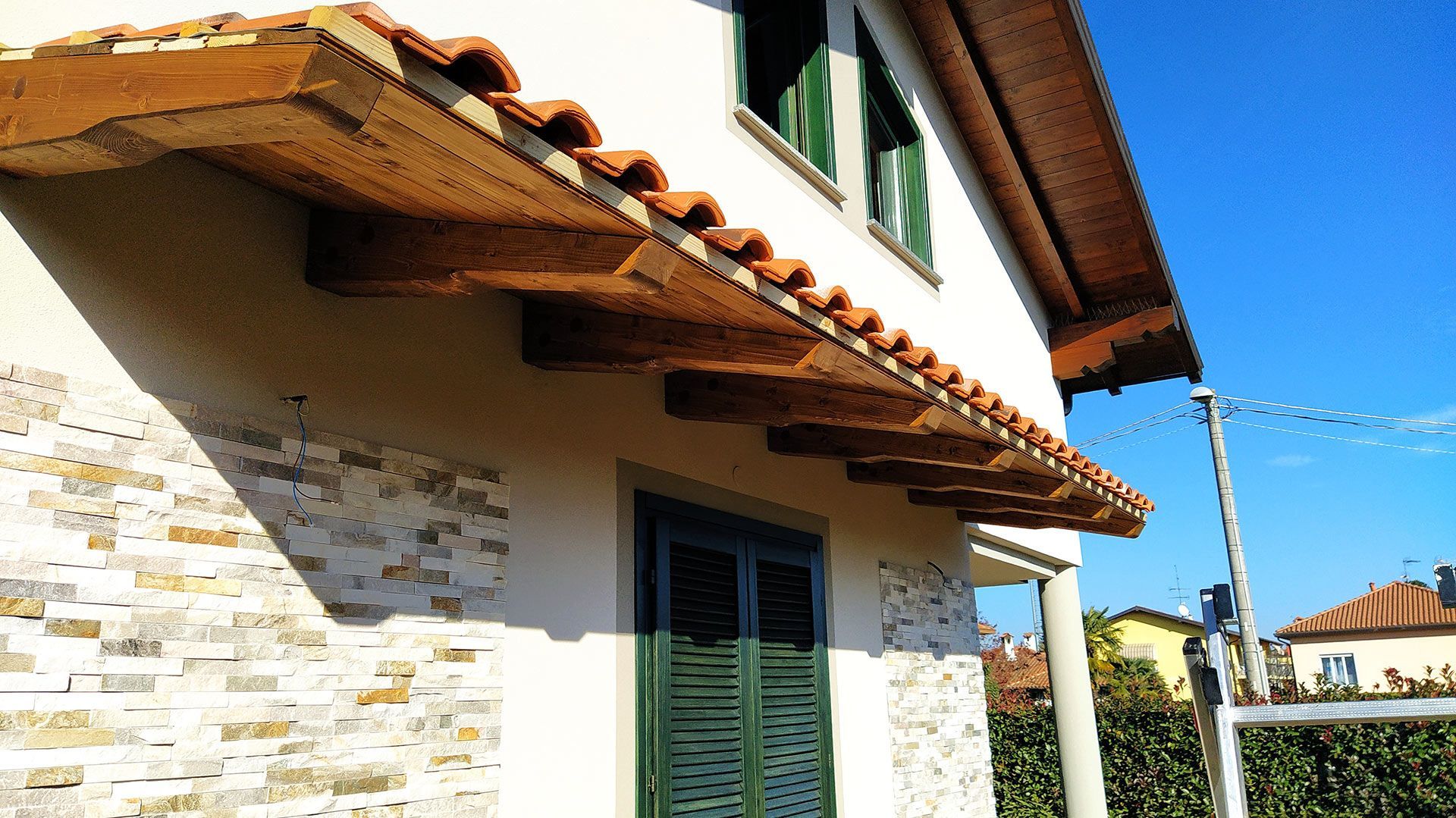 Casa bianca con tegole in terracotta e persiane verdi sotto un cielo azzurro brillante