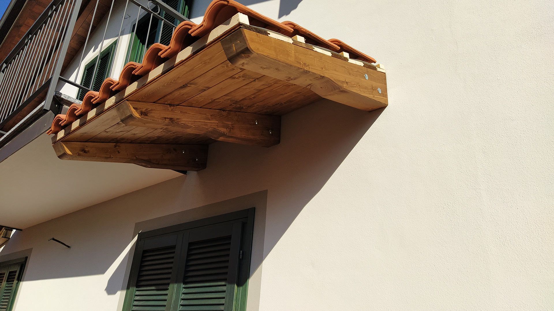 Balcone con ringhiera in legno e piante in vaso sulla facciata dell'edificio in stucco color crema.