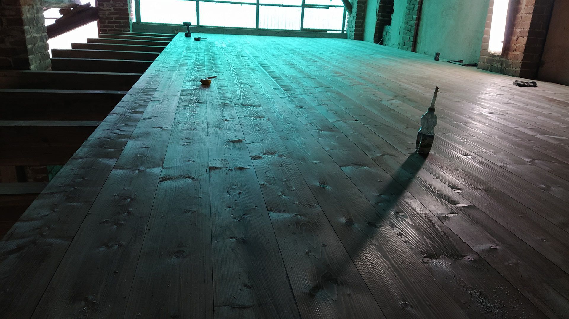 Pavimento in legno scarsamente illuminato in una stanza vuota, con la luce del sole che filtra attraverso una porta a vetri.