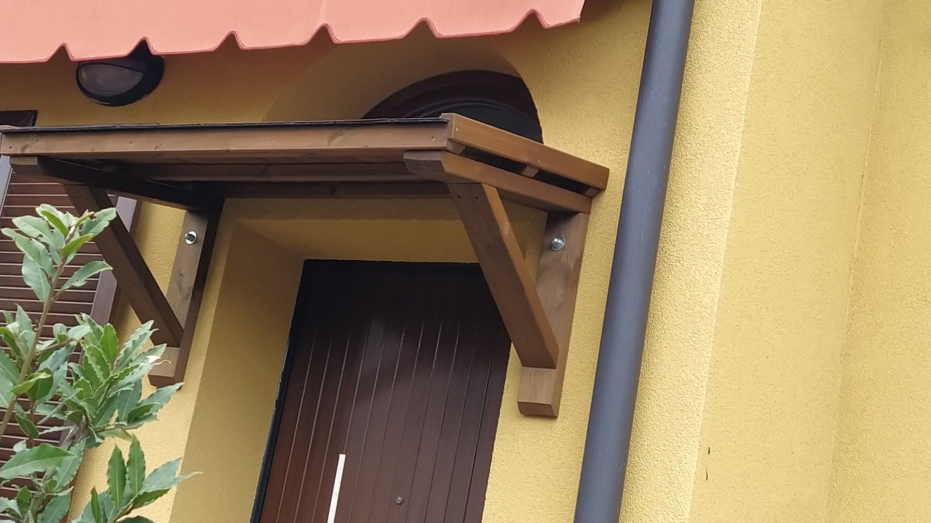 Tenda da sole in legno sopra una porta scura su una parete esterna gialla