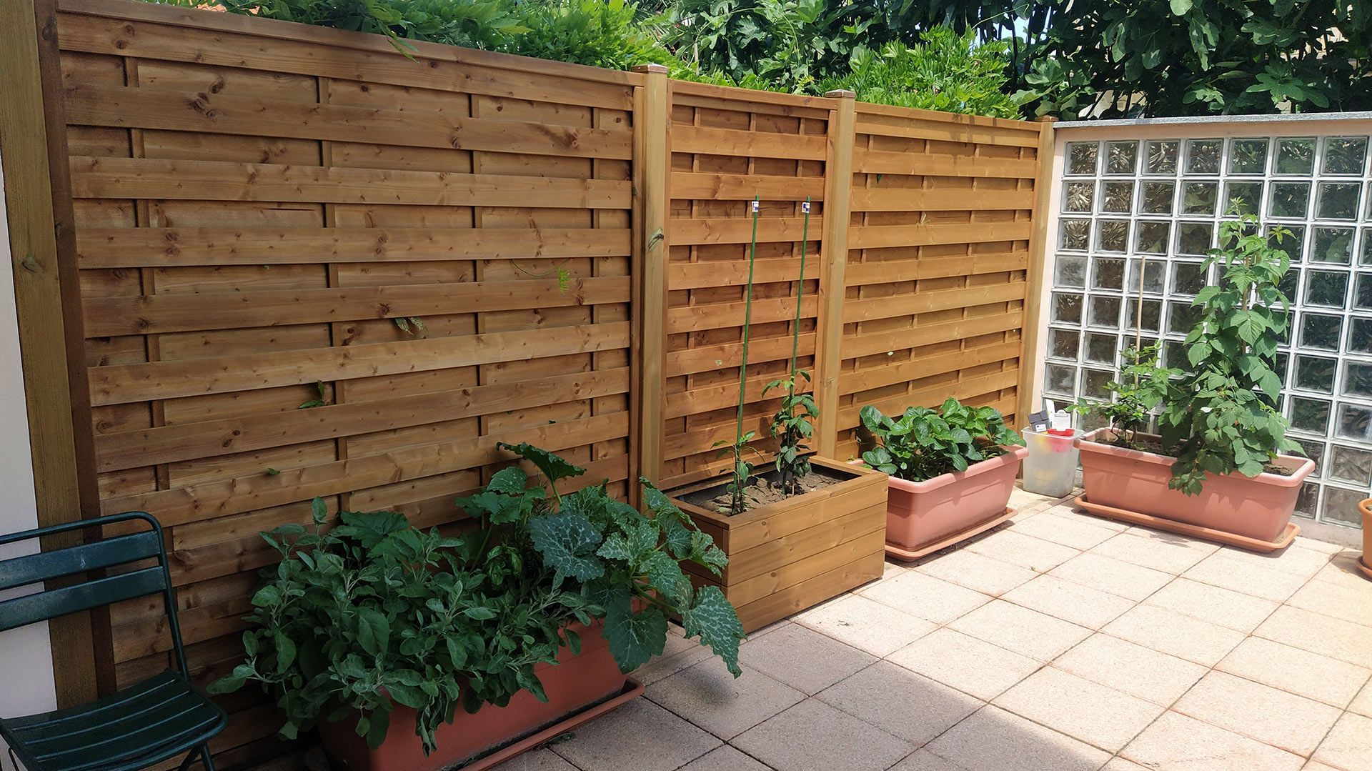 Angolo del patio con recinzione in legno, pavimento piastrellato e piante in vaso lungo il muro.