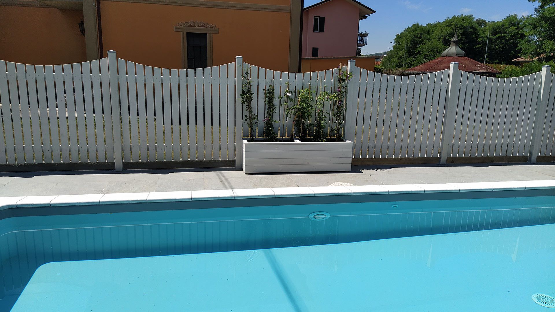 Piscina nel cortile sul retro con acqua turchese, recinzione bianca e fioriera davanti a una casa