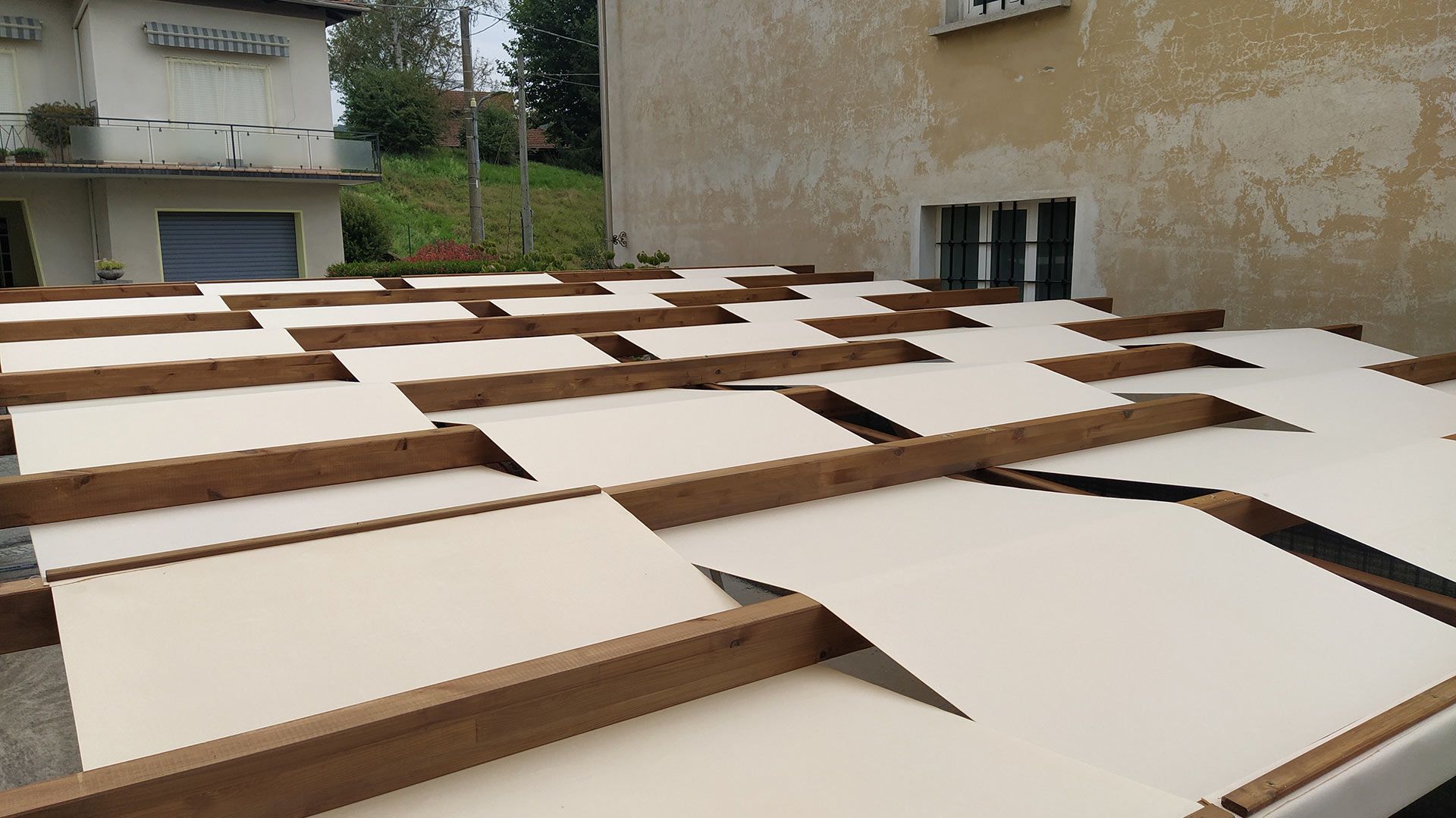 Pile di fogli di cartone piatti, con bordi marroni e parte superiore bianca, disposte all'aperto tra gli edifici.