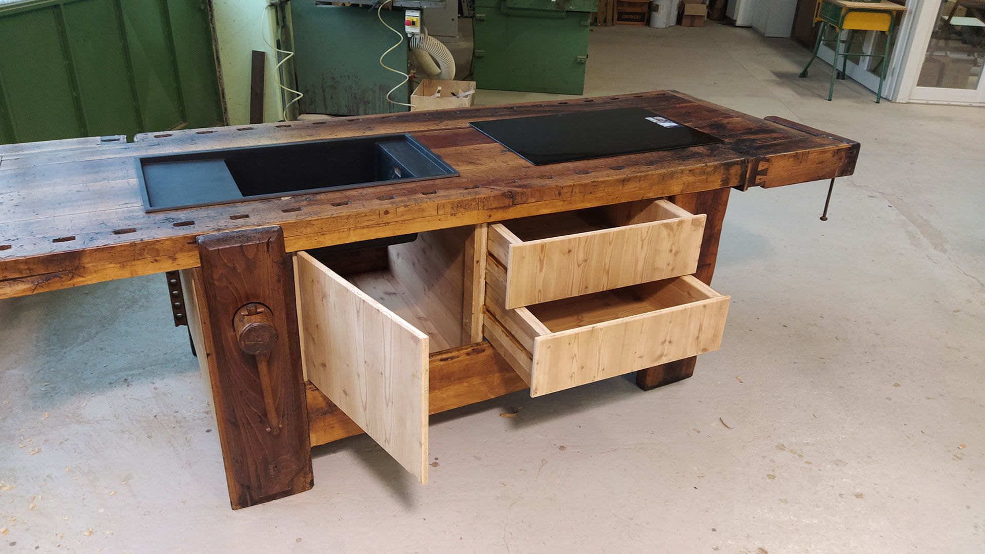 Banco da lavoro rustico in legno con cassetti a vista e piano intarsiato scuro in un'officina.