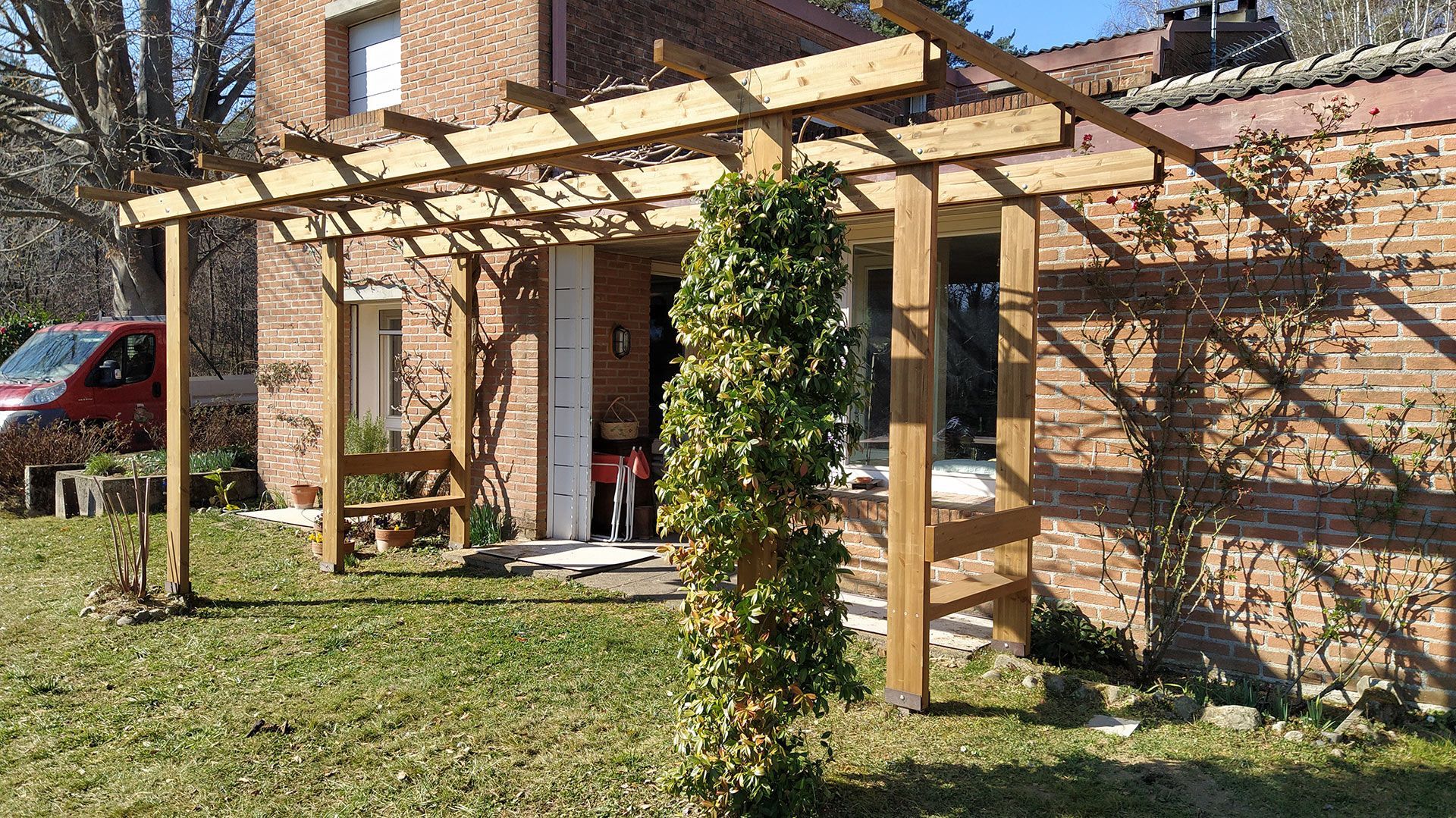 Ingresso di una casa in mattoni con pergolato in legno e un piccolo cortile anteriore soleggiato