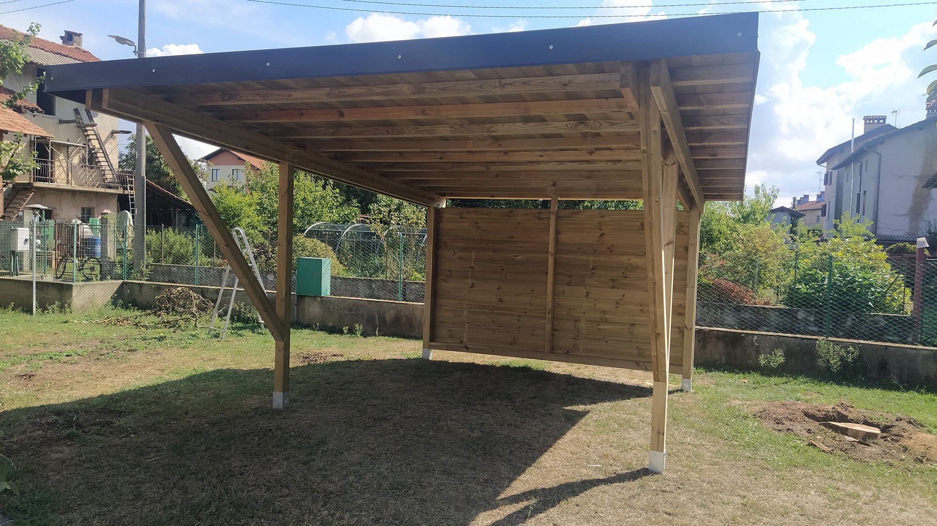 Semplice riparo in legno aperto sui lati con tetto ondulato in un cortile erboso.