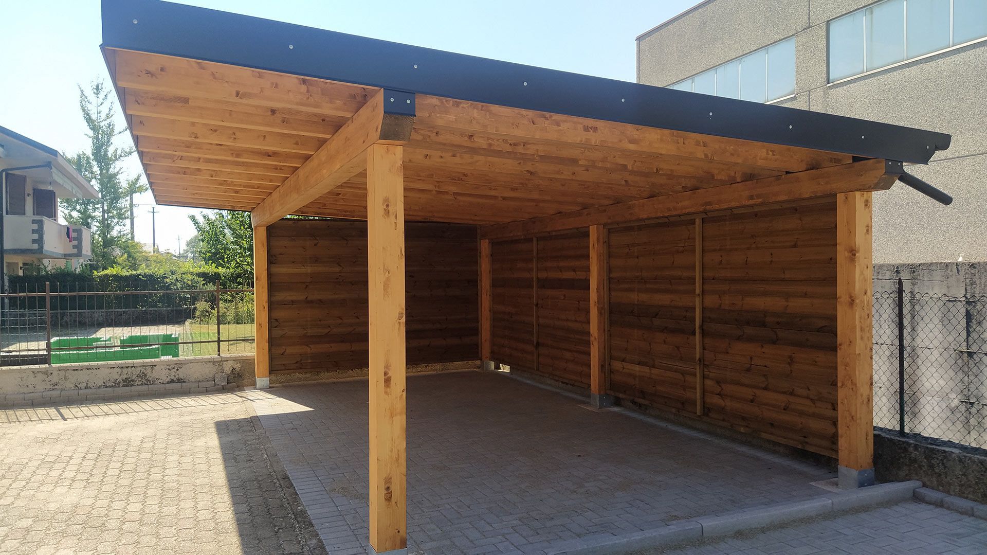 Tettoia in legno per esterni con tetto inclinato e lati aperti, su una superficie pavimentata.