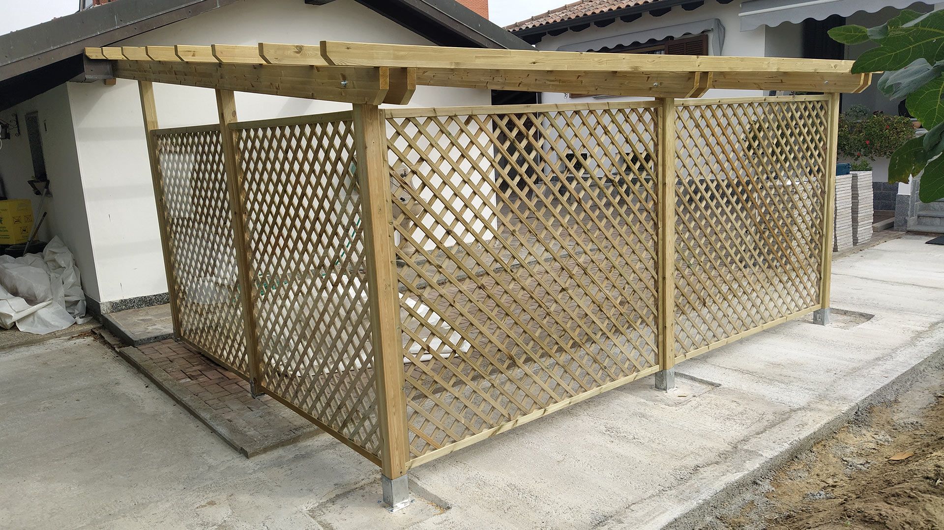 Recinzione in legno a traliccio accanto a una casa su una lastra di cemento.