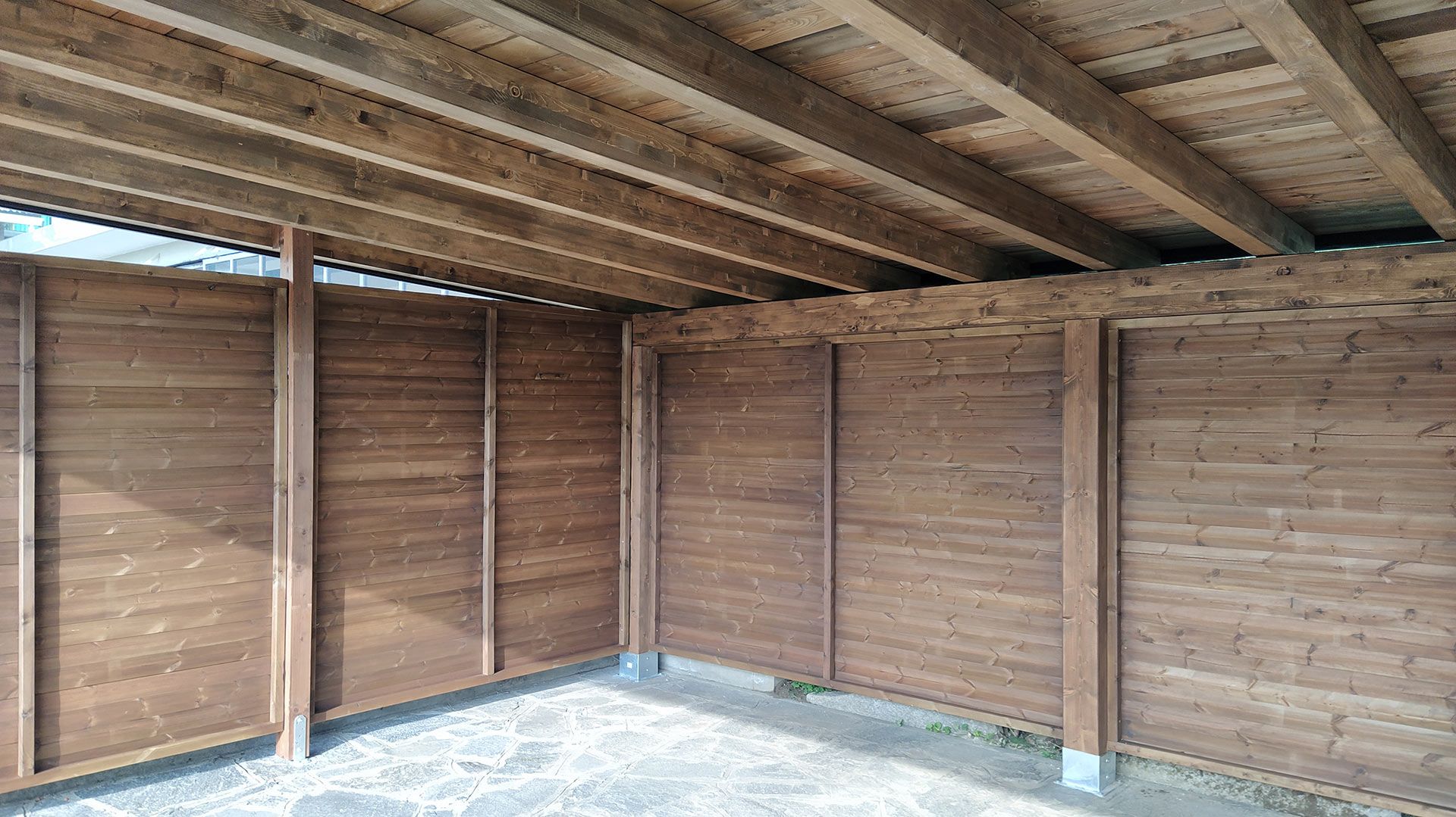 Interno di un capannone di legno vuoto con travi a vista e pavimento in cemento.