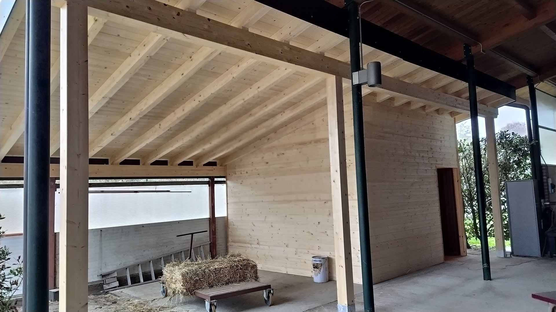 Patio coperto con travi in legno e una piccola struttura in mattoni accanto a un muro e zona salotto esterna.